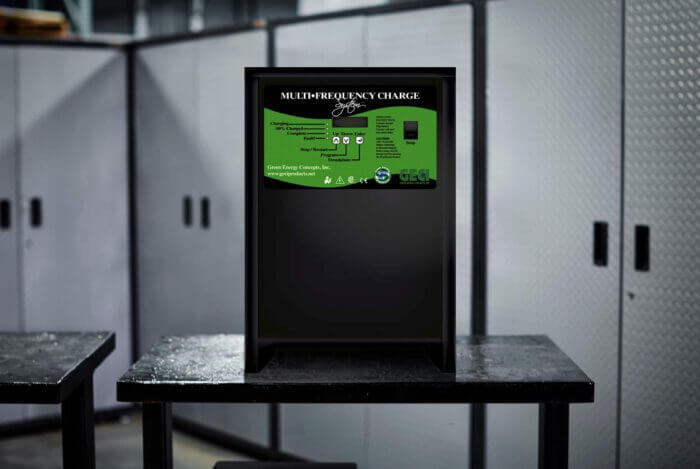 A black GECI Multi-Frequency Charge System with a green control panel faceplate, positioned on a workbench in a workshop setting.
