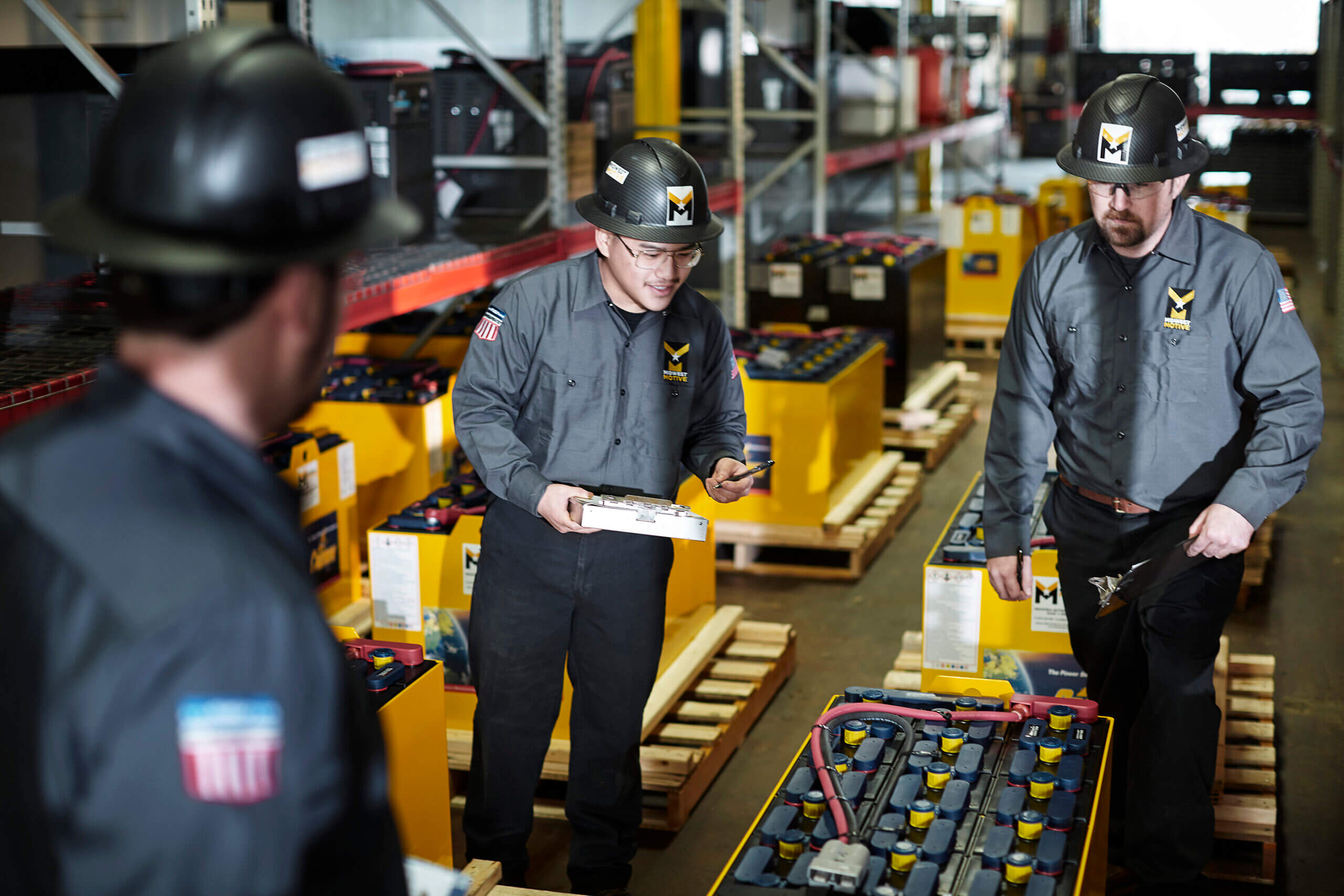 Three workers inspecting industrial batteries in a warehouse setting
