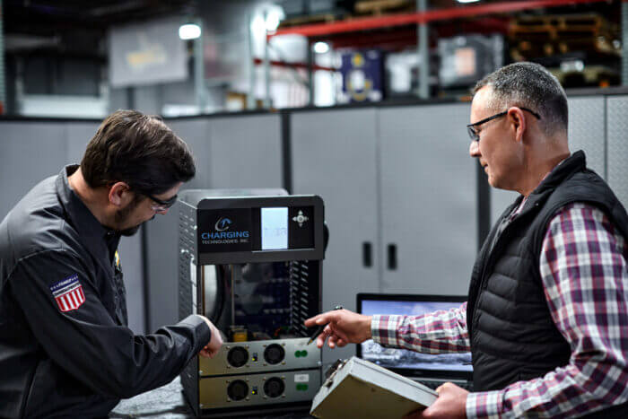 Workers inspecting and adjusting an industrial battery charger